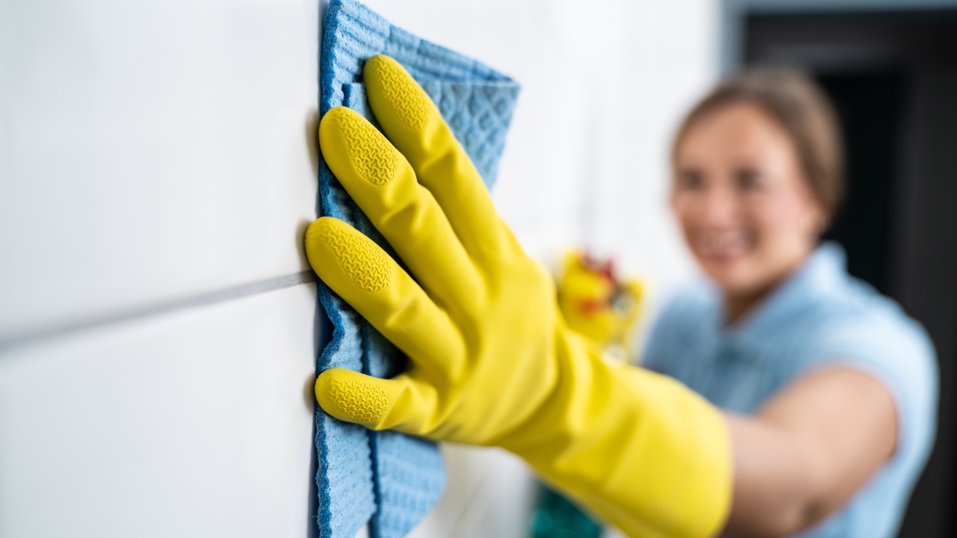 A woman wearing yellow gloves is cleaning a wall